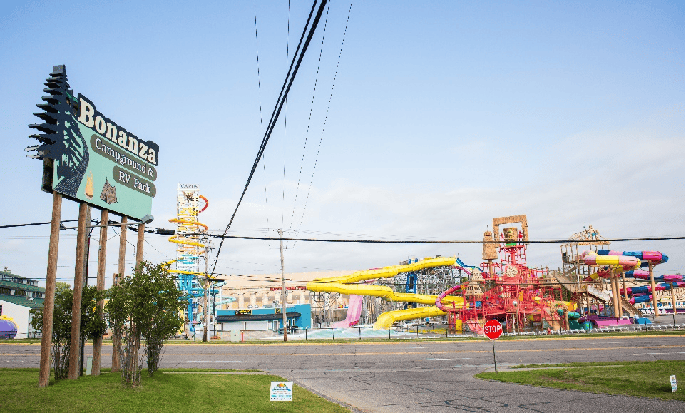 Large outdoor water park with colorful slides is visible behind a sign reading “Bonanza Campground & RV Park” on a sunny day.