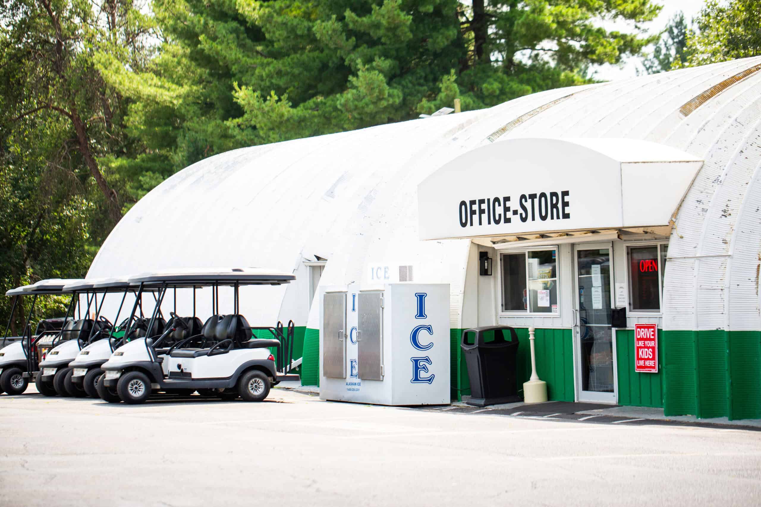 White building marked "Office-Store" with an ice machine and golf carts parked outside; trees in the background.