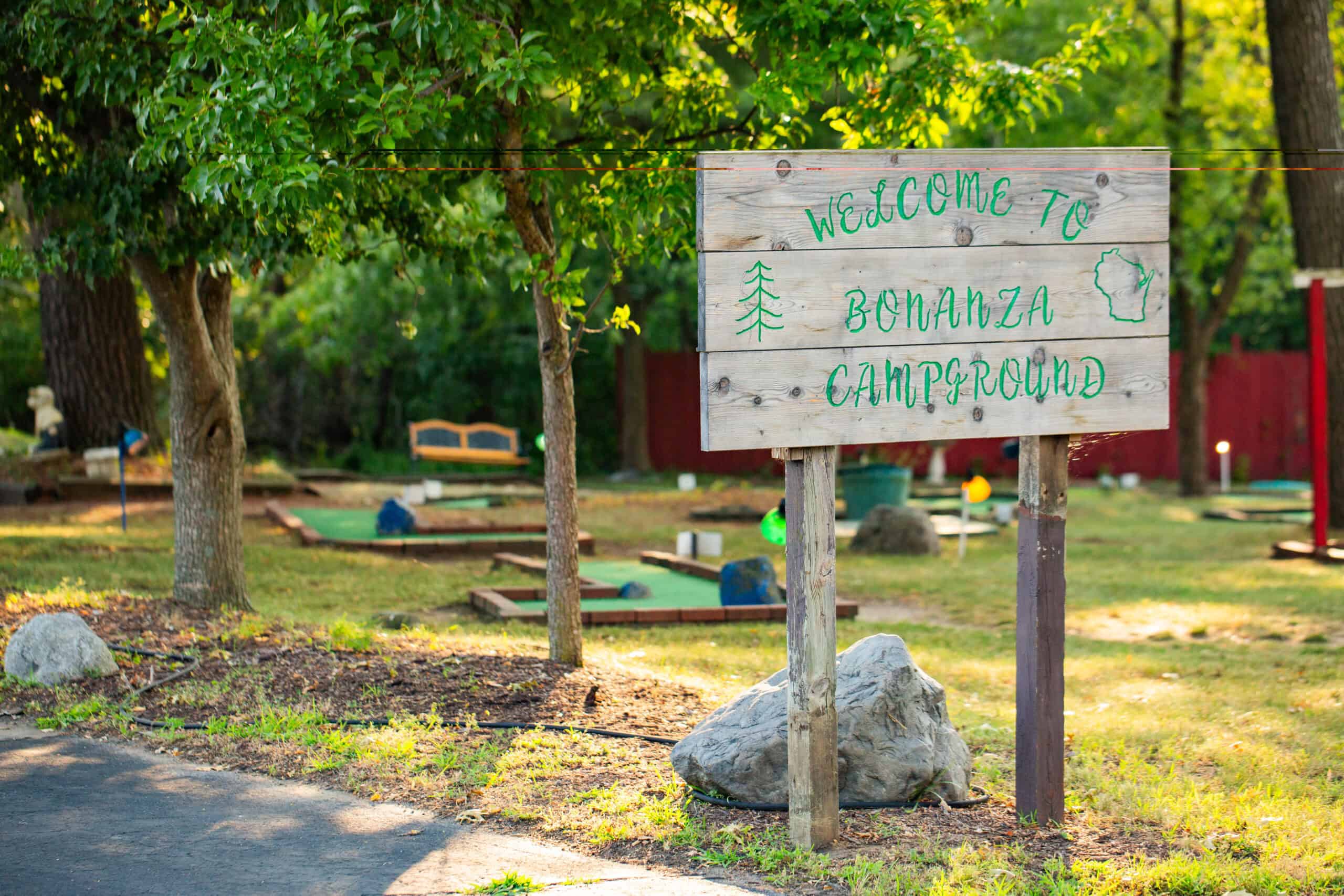A wooden sign reads "Welcome to Bonanza Campground" surrounded by trees and a mini-golf course in the background.