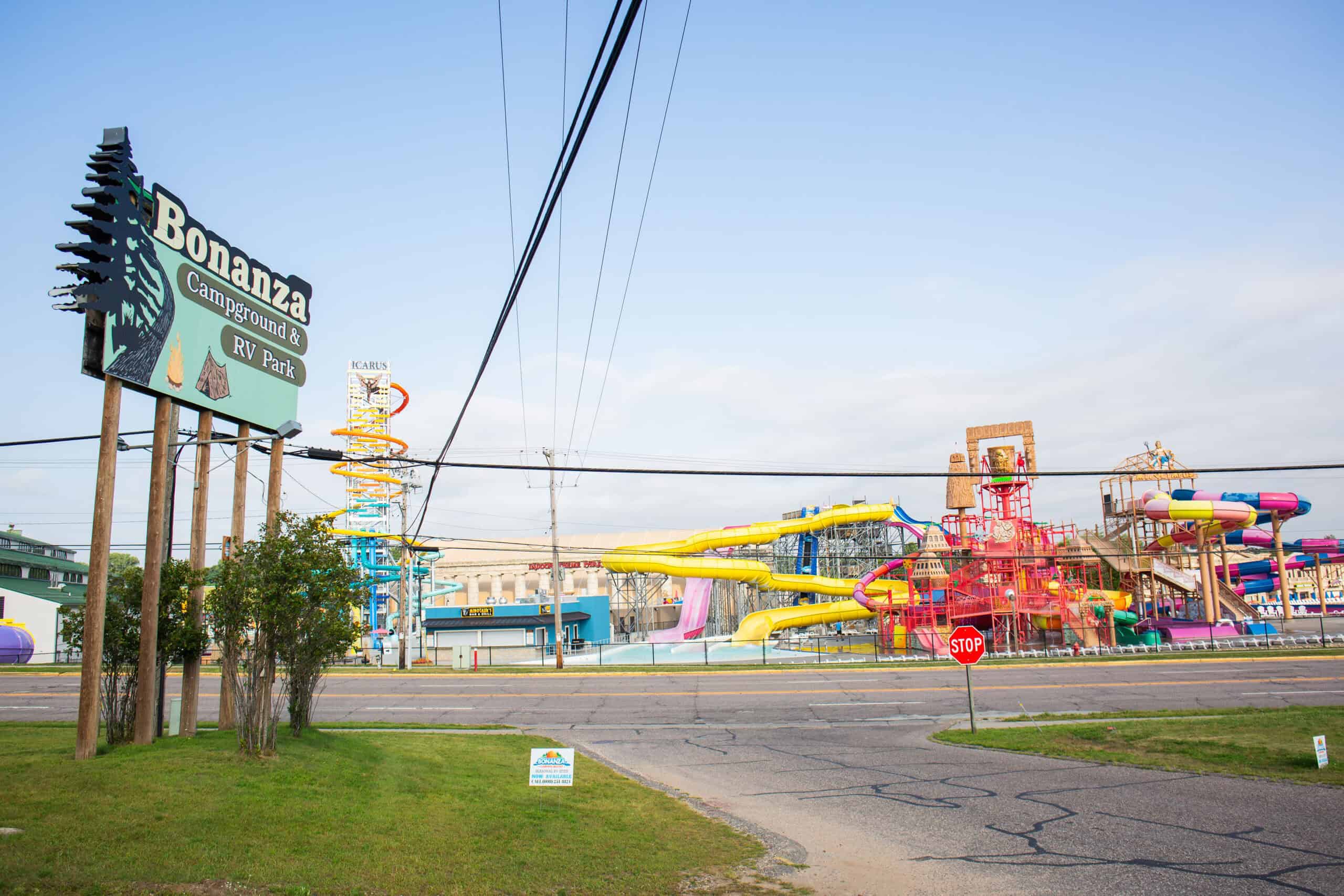 Bonanza Campground & RV Park sign in front of a colorful water park with slides and structures, seen across a street with a stop sign.